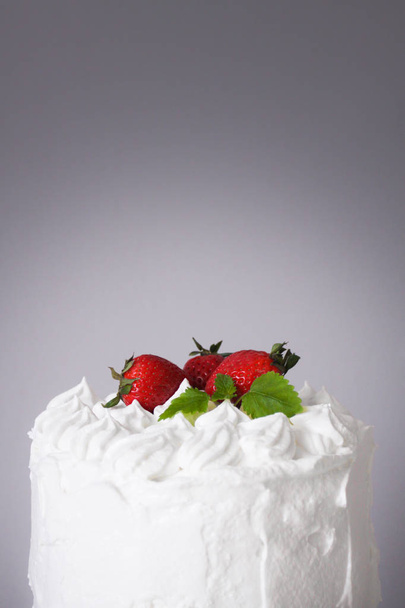 Large white delicious cake with cream and decorated with strawberries and mint on a transparent stand on a gray background   - Фото, изображение
