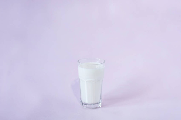 glass of fresh milk in the center of the frame on a lavender background - Fotoğraf, Görsel