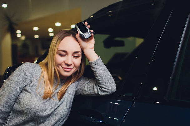 Happy woman holding keys to her new car at the dealership. - Fotoğraf, Görsel