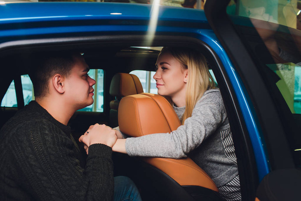 Podejmowanie decyzji. Piękna kochająca para siedzi w nowym samochodzie razem w salonie przystojny człowiek i jego kochająca dziewczyna wybierając samochód razem konsumpcjonizm pojazdu. - Zdjęcie, obraz