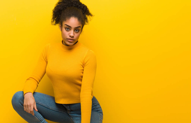 Young black woman sitting over an orange wall - Photo, image