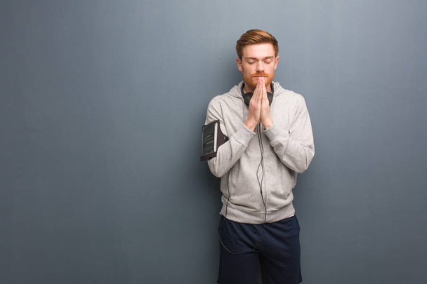 Jonge fitness roodharige man bidden zeer gelukkig en vol vertrouwen - Foto, afbeelding