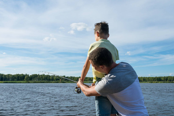 dad teaches son to fish on spinning on the lake, rear view - Foto, Imagen