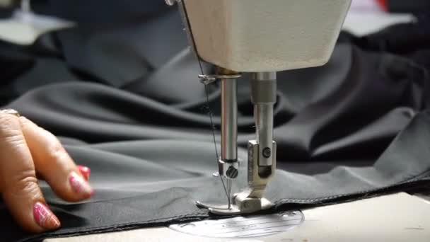 Primer plano del sastre. Las manos femeninas de una costurera en el trabajo. Costura con una máquina de coser con material negro. Industria de la moda
. - Metraje, vídeo