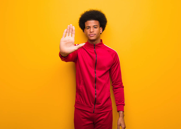 junger, sportlicher schwarzer Mann über orangefarbener Wand, der die Hand vor die Nase hält - Foto, Bild