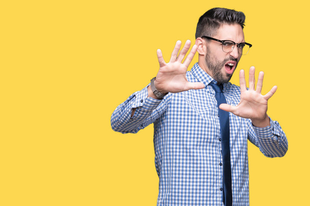 Young business man wearing glasses over isolated background afraid and terrified with fear expression stop gesture with hands, shouting in shock. Panic concept. - Photo, Image