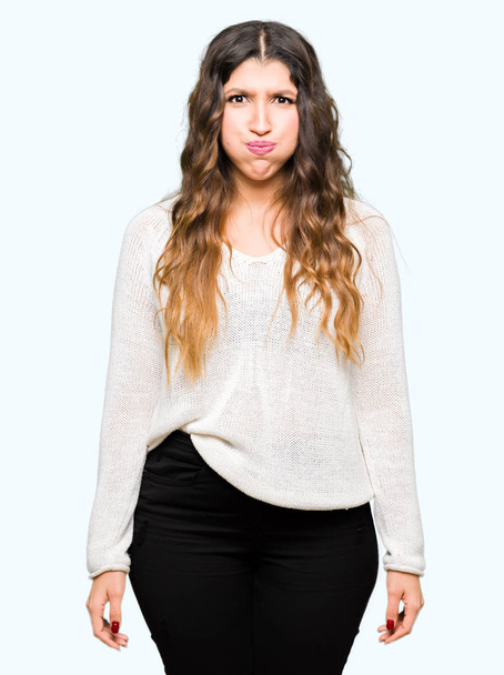 Young beautiful woman wearing white sweater puffing cheeks with funny face. Mouth inflated with air, crazy expression. - Photo, Image