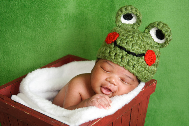 újszülött fiú zöld horgolt béka kalapban. alszik egy piros fadobozban. - Fotó, kép