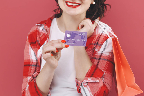 Portrait of happy nice girl with curly hair holding bags and credit card after shopping - Photo, image