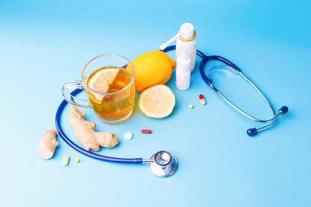 Cold preparations, stethoscope, tea, lemon and ginger root on a blue background. - Фото, изображение