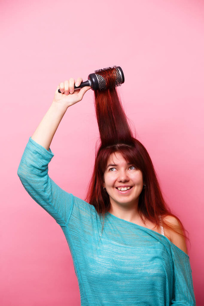 Γυναίκα βούρτσισμα τα μαλλιά της σε ροζ φόντο - Φωτογραφία, εικόνα