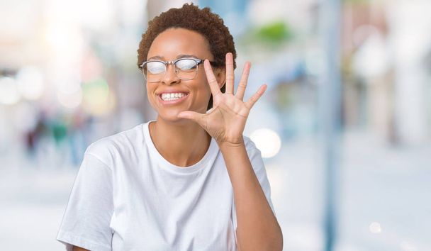 Όμορφη νεαρή αφρικανική αμερικανική γυναίκα φοράει γυαλιά πέρα από το απομονωμένο υπόβαθρο δείχνει και δείχνει προς τα επάνω με τα δάχτυλα αριθμός πέντε ενώ χαμογελώντας αυτοπεποίθηση και χαρούμενοι. - Φωτογραφία, εικόνα