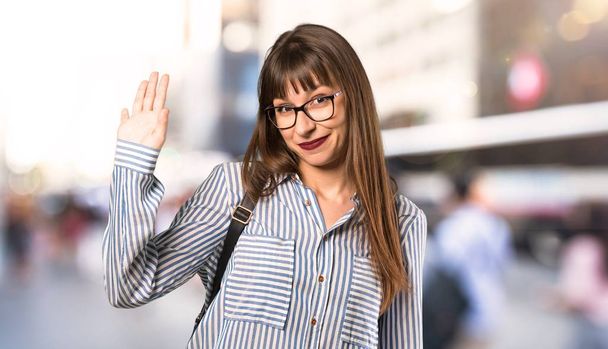 Γυναίκα με γυαλιά χαιρετούν με το χέρι με ευτυχισμένο έκφραση σε εξωτερικούς χώρους - Φωτογραφία, εικόνα