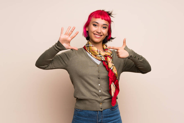 Молода жінка з рожевим волоссям над жовтою стіною рахує сім з пальцями
 - Фото, зображення