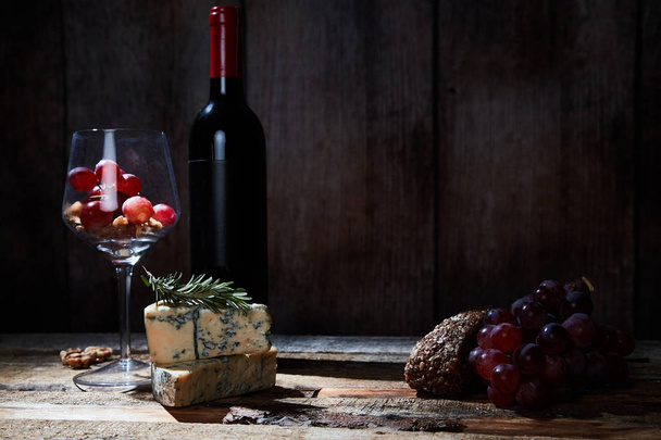 Gourmet composition of wineglass with grapes and walnuts on wood table with cheese and bottle of red wine. Copy space - Fotoğraf, Görsel