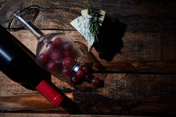 Wineglass with grapes on wood table with blue cheese and bottle of red wine. Top view - Φωτογραφία, εικόνα