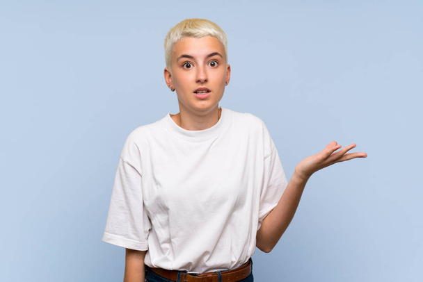Menina adolescente com cabelos brancos curtos sobre a parede azul fazendo gestos de dúvidas
 - Foto, Imagem