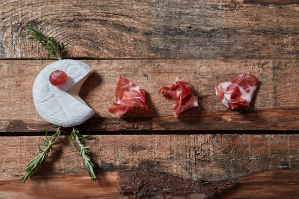 Arrangement of gourmet assorted appetizers of cheese and prosciutto on wooden surface. Top view - Photo, image