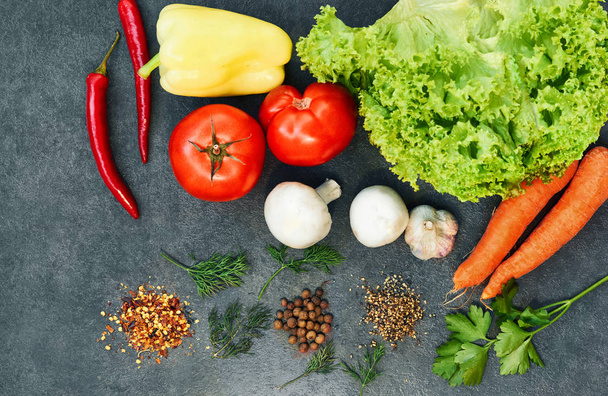 Healthy food background. Healthy food concept with fresh vegetables and ingredients for cooking. Top view with copy space. Aromatic herbs, onion, pepper, cucumber,lettuce, carrots, mushrooms, tomatoes, garlic. Dark background - Photo, Image