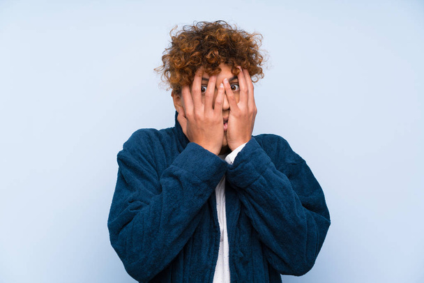 Young african american man in pajamas covering eyes and looking through fingers - 写真・画像