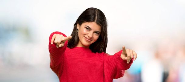 Teenager girl with red sweater points finger at you while smiling at outdoors - Foto, Imagem