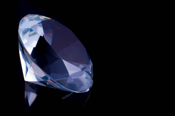 ein riesiger Diamant auf einer schwarzen Spiegeloberfläche, ein Spiegelbild eines Diamanten. - Foto, Bild