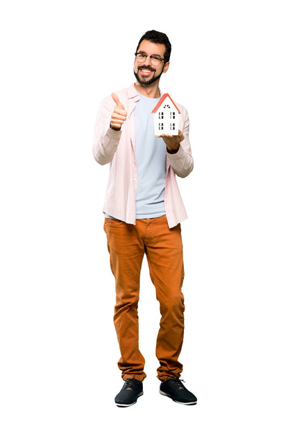 Full-length shot of Handsome man with beard holding a little house over isolated white background - Foto, Imagem