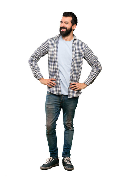 Handsome man with beard posing with arms at hip and smiling over isolated white background - Φωτογραφία, εικόνα