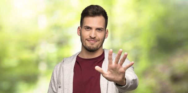 Άντρας με πουλόβερ που μετράει πέντε με δάχτυλα σε ένα πάρκο - Φωτογραφία, εικόνα