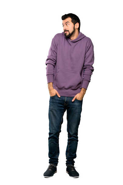 Full-length shot van knappe man met Sweatshirt maken twijfels gebaar op zoek naar kant over geïsoleerde witte achtergrond - Foto, afbeelding
