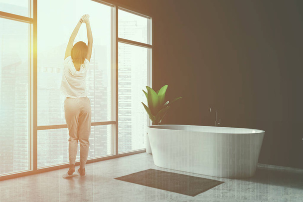 Woman in black bathroom with white tub - Foto, Bild
