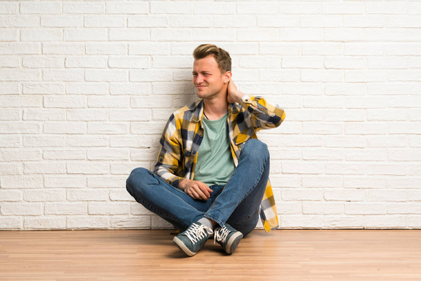 Blonde man zittend op de vloer met neckache - Foto, afbeelding