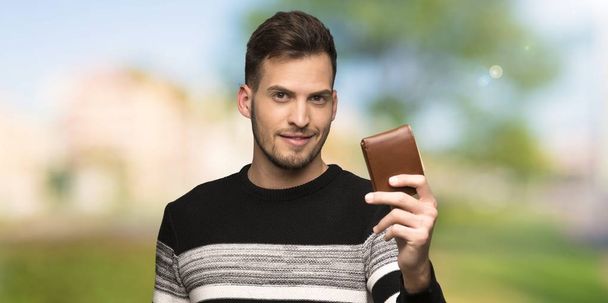 Hombre guapo sosteniendo una billetera al aire libre
 - Foto, Imagen