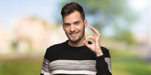 Όμορφος άνθρωπος δείχνει OK πινακίδα με τα δάχτυλα σε εξωτερικούς χώρους - Φωτογραφία, εικόνα