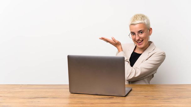 Chica adolescente con el pelo corto con un ordenador portátil que presenta una idea mientras mira sonriendo hacia
 - Foto, Imagen