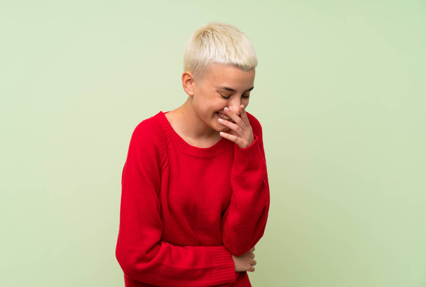 Teenagerka s bílými krátkými vlasy na zelené stěně se hodně usmívá - Fotografie, Obrázek