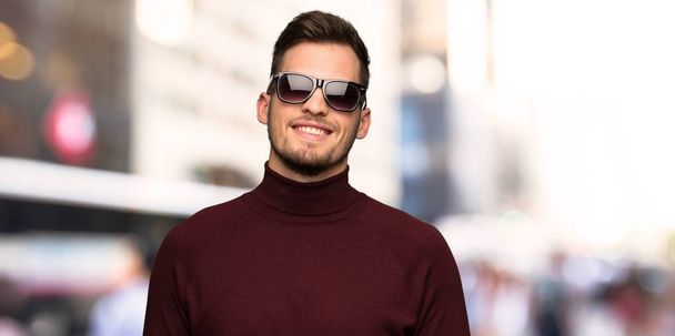 Hombre con jersey de cuello alto con gafas y feliz en la ciudad
 - Foto, Imagen