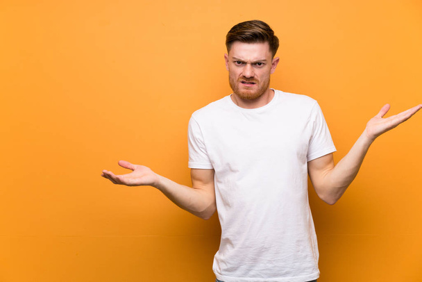 Redhead man over brown wall unhappy for not understand something - Zdjęcie, obraz