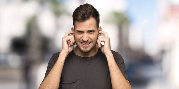 Чоловік з чорною сорочкою розчарований і прикриває вуха руками на відкритому повітрі
 - Фото, зображення