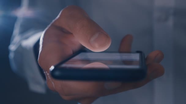 Männliche Hand blättert nachts auf einem großen schwarzen Smartphone durch die Nachrichten - Filmmaterial, Video