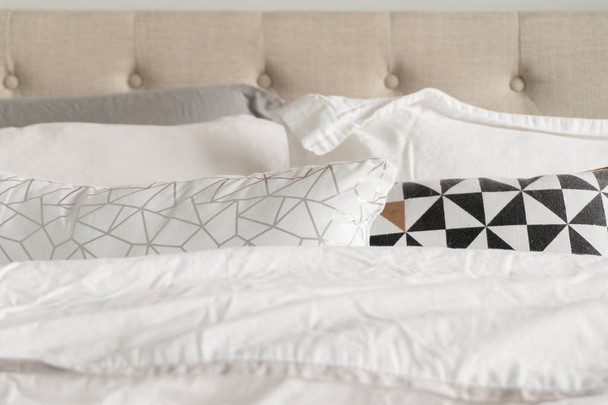 グレー、ホワイト、ブラック、ゴールド、ホワイトの寝具付きの装飾的な寝具枕。ベージュファブリックは、背景にヘッドボードをタフト。ふわふわで快適に見えるベッドクローズアップ. - 写真・画像