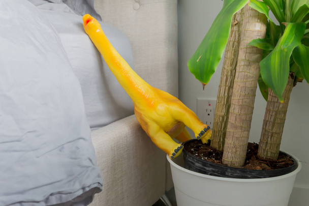 Žlutý hračka dinosaurus spadl na bok postele, v květináči, zobrazující rodinný domov a rodičovský život. - Fotografie, Obrázek