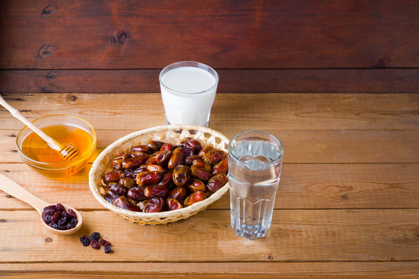 Dried dates, milk and honey on wooden background. Holy month of Ramadan, concept. Righteous Muslim lifestyle. Starvation. Dates in a wooden basket and raisins in the style of minimalism - Photo, Image