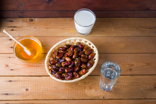Dried dates, milk and honey on wooden background. Holy month of Ramadan, concept. Righteous Muslim lifestyle. Starvation. Dates in a wooden basket and raisins in the style of minimalism - Fotoğraf, Görsel