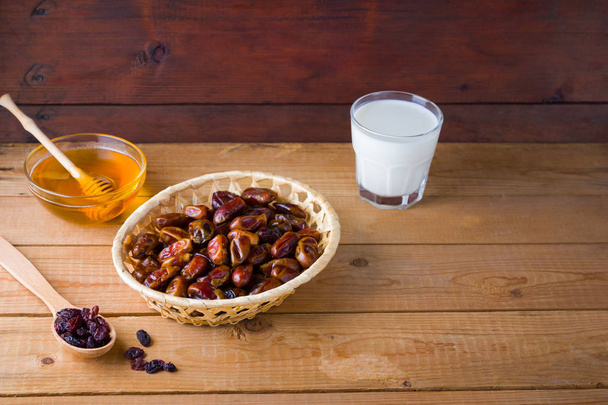 Dried dates, milk and honey on wooden background. Holy month of Ramadan, concept. Righteous Muslim lifestyle. Starvation. Dates in a wooden basket and raisins in the style of minimalism - Foto, Bild