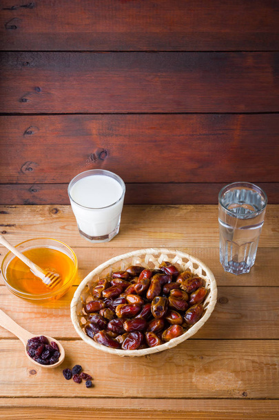 Dried dates, milk and honey on wooden background. Holy month of Ramadan, concept. Righteous Muslim lifestyle. Starvation. Dates in a wooden basket and raisins in the style of minimalism - Foto, Imagen