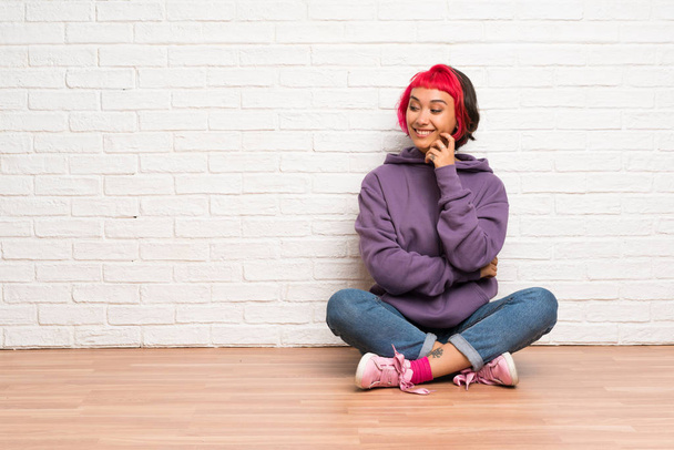 Young woman with pink hair sitting on the floor looking to the side - Fotó, kép