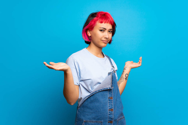 Young woman with pink hair over blue wall unhappy for not understand something - Photo, Image