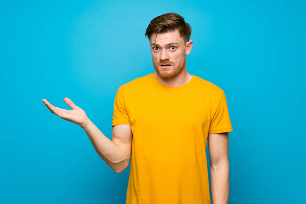 Redhead man over blue wall making doubts gesture - Photo, Image