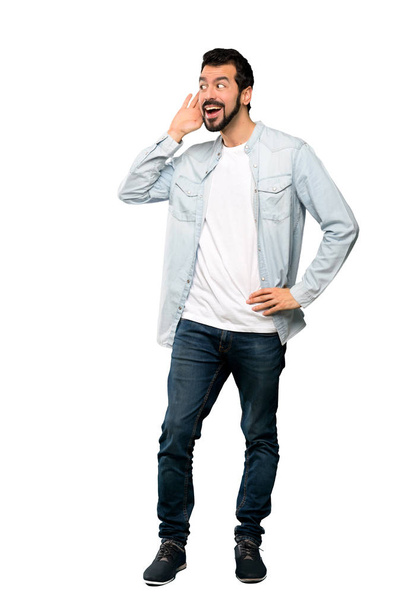 Full-length shot of Handsome man with beard listening to something by putting hand on the ear over isolated white background - Foto, afbeelding